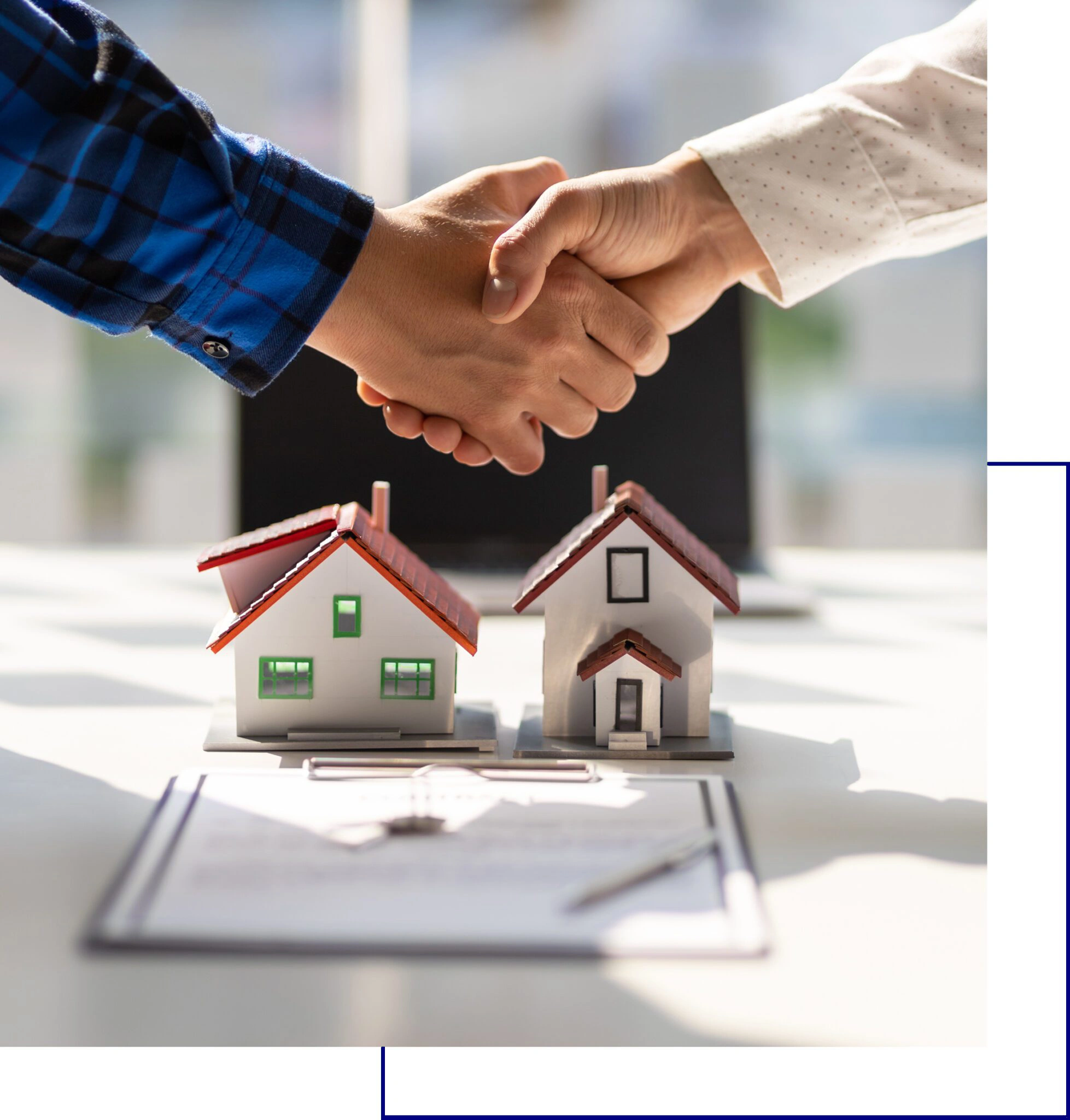 Two people shaking hands over miniature house models and contract papers.